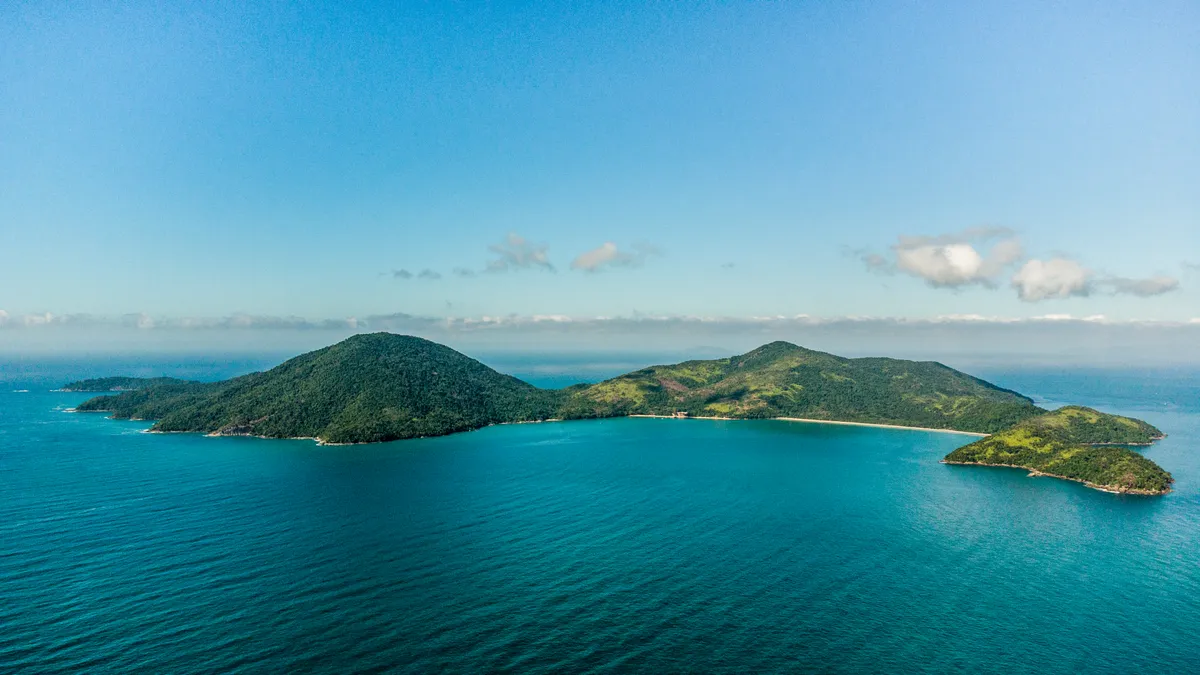 Vista aérea da Ilha Anchieta em Ubatuba cercada por água azul e coberta de Mata Atlântica